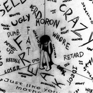 Hand drawn depiction of a girl huddled in a corner surrounded by derogatory words scratched angrily into the walls and ceiling. Some of the words included are ugly, dumb, freak, crazy, loser and whore.