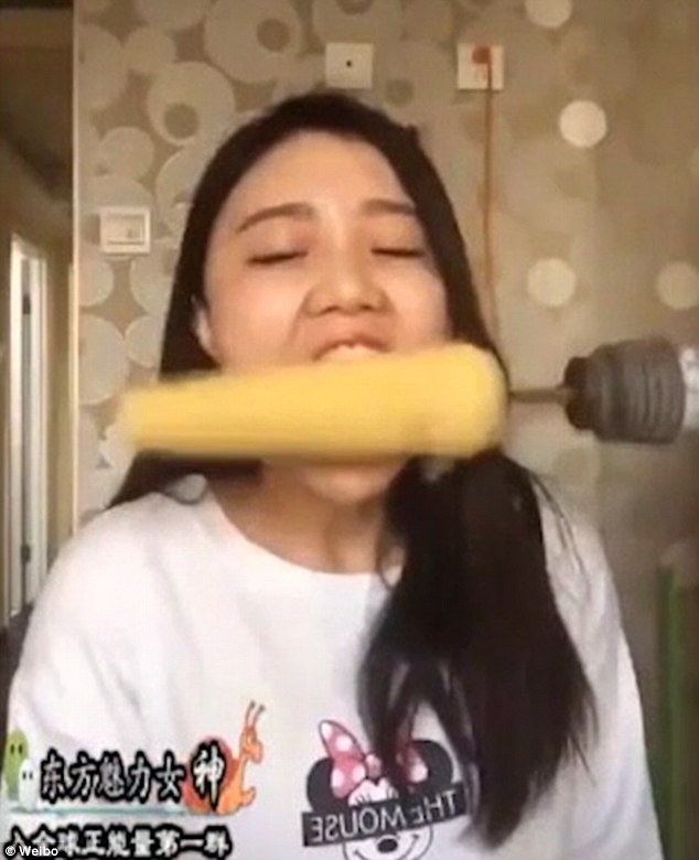 The woman puts her teeth against the rotating cob of corn without considering tucking away her long locks