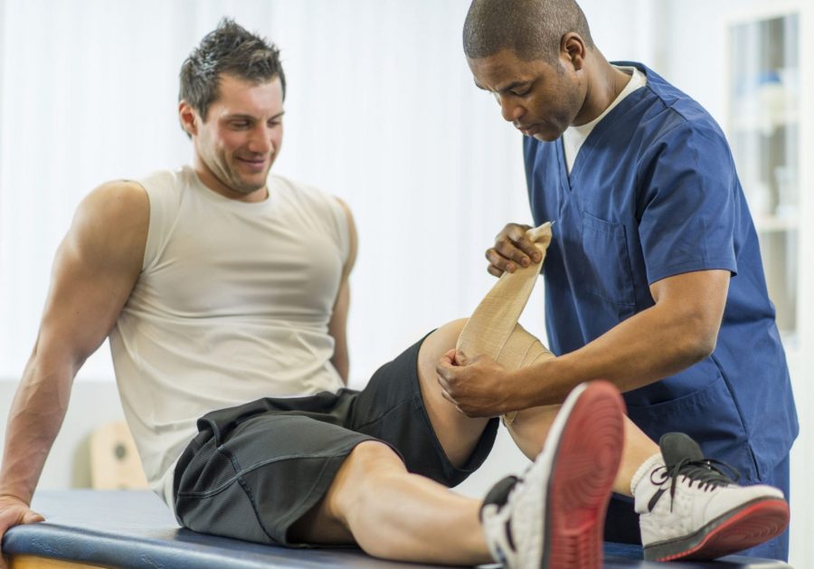 Спортивный врач разминает атлету колено на кушетке