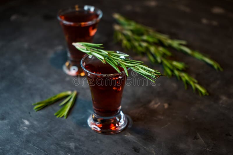 Cherry, berry tincture on a dark background, with a sprig of rosemary. Cherry, berry and spicy tincture of alcohol and berries in the glasses. on a dark royalty free stock image
