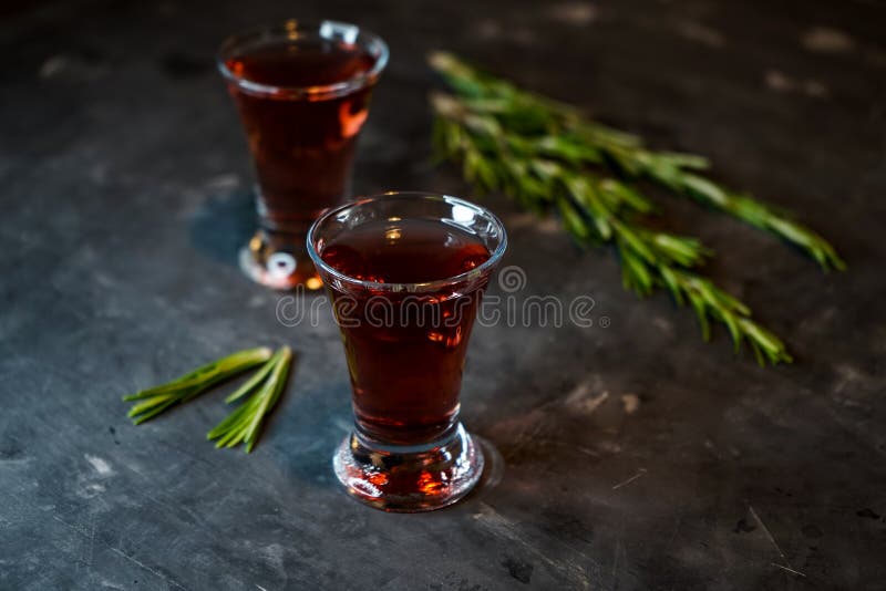 Cherry, berry tincture on a dark background, with a sprig of rosemary. Cherry, berry and spicy tincture of alcohol and berries in the glasses. on a dark royalty free stock images