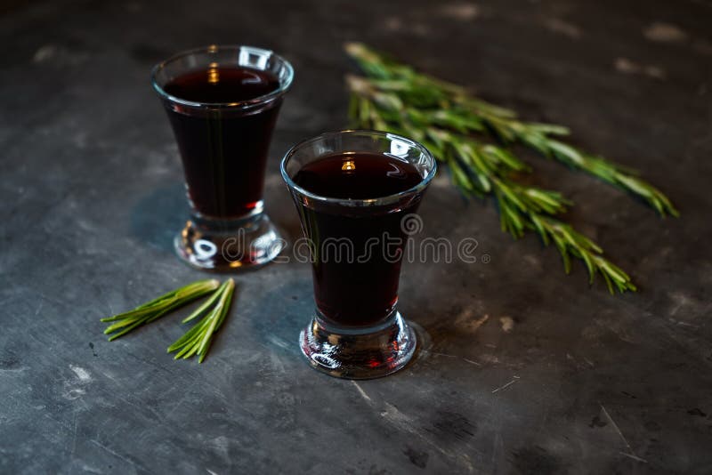 Cherry, berry tincture on a dark background, with a sprig of rosemary. Cherry, berry and spicy tincture of alcohol and berries in the glasses. on a dark stock photos