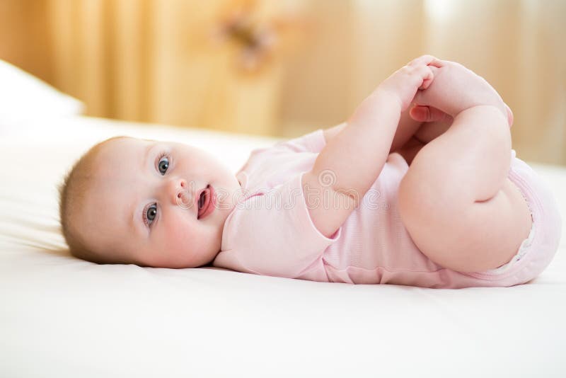 Concept of healthy child. Cute baby lying on her back on bed in room, holding legs with her hands. The concept of a healthy child. Cute baby lying on her back stock photography
