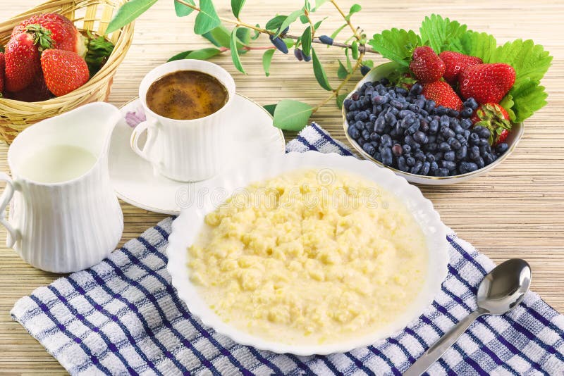 Corn porridge with milk, a Cup of coffee and the berries of honeysuckle and strawberry on the table royalty free stock photography