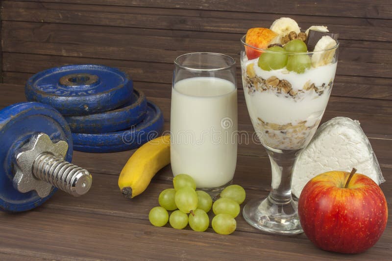 Diet for athletes build muscle mass. Protein snack. Dairy products and dumbbells. Fresh milk in the glass and muesli breakfast on a wooden table. Oatmeal with royalty free stock images