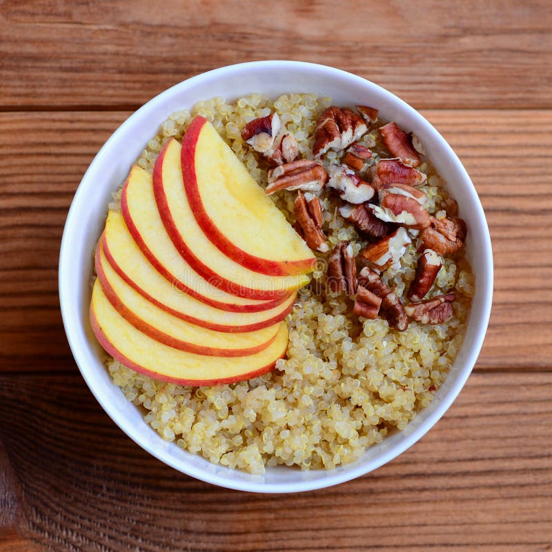 Fruit and nut Breakfast quinoa porridge. Quinoa porridge with fresh apples and pecans in a white bowl isolated on wood background royalty free stock image