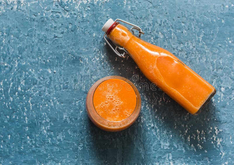 Glass and takeaway bottle with vitamin mango magic smoothies on a blue background, top view.  Smoothies with ripe mango, carrot,. Glass and takeaway bottle with stock photos