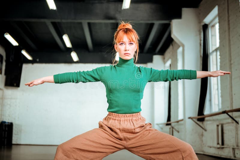 Good-looking slim yoga coach in a green turtleneck doing exercises for strong legs. Exercises for legs. Good-looking slim yoga coach wearing a green turtleneck royalty free stock photo