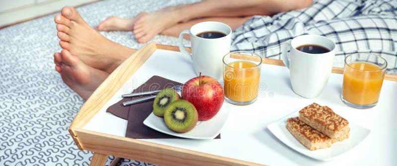 Healthy breakfast on tray and couple legs in background. Closeup of healthy breakfast served on a wooden tray ready to eat and couple legs over a bed in the stock photography