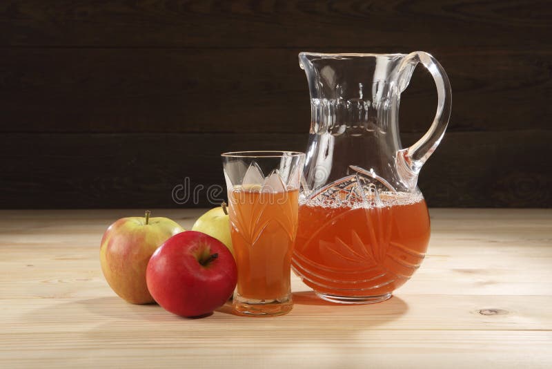 Healthy food. A jug with freshly squeezed apple juice near ripe apples and a crystal glass on a wooden table. A background of old, stock photos