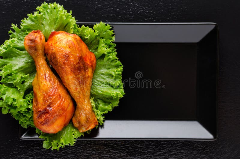 Healthy grilled chicken legs with fresh lettuce on black background. Flat lay stock photography