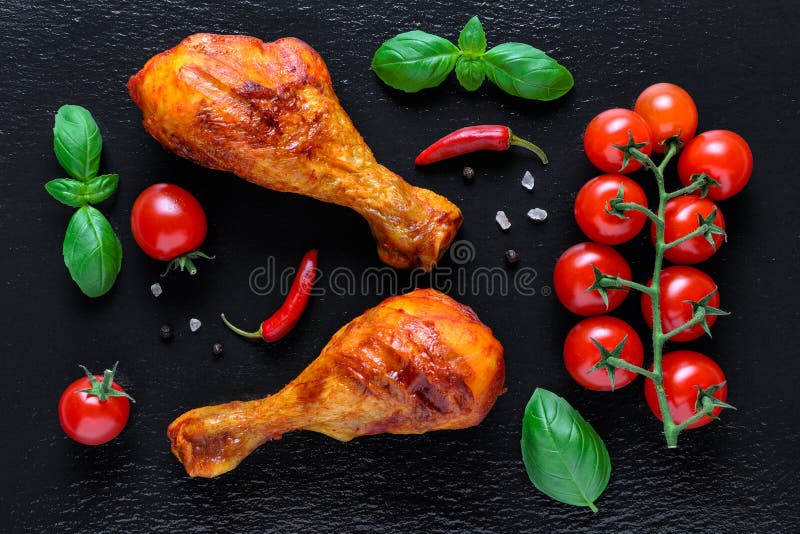Healthy grilled chicken legs with fresh tomato, basilik and chili on black background. Flat lay royalty free stock photo