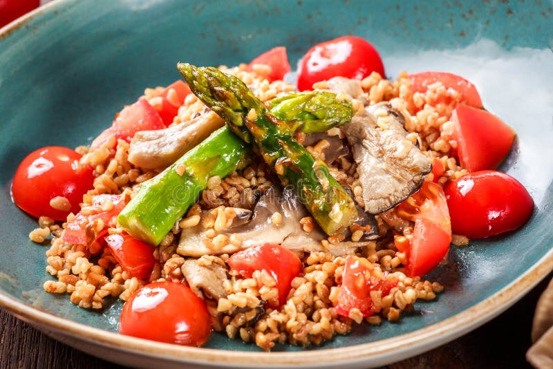 Healthy salad of barley porridge with asparagus, tomatoes and mushrooms on plate. Vegan food. Top view royalty free stock image