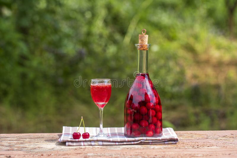 Homemade tincture of red cherry. Berry alcoholic drinks concept. Red wine made in a glass bottle and a wineglass. Homemade tincture of red cherry. Berry stock photo