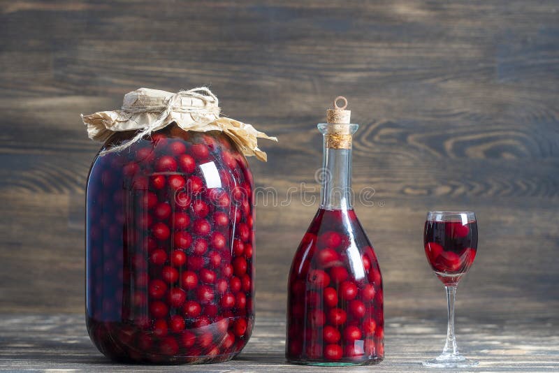 Homemade tincture of red cherry in a glass bottle, jar and a wineglass on wooden background, Ukraine, close up. Berry alcoholic drinks concept royalty free stock photography