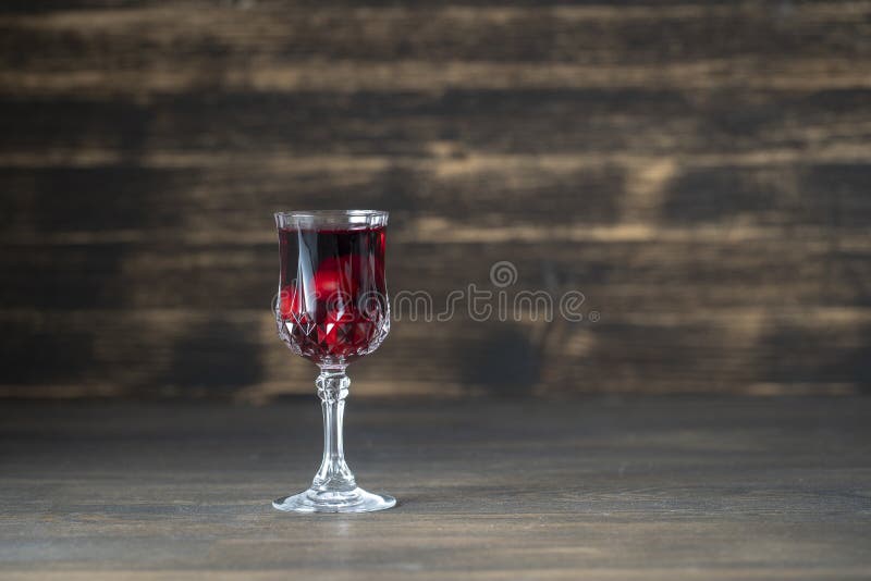 Homemade tincture of red cherry in a wine crystal glass on wooden background, Ukraine. Close up, copy space. Berry alcoholic drinks concept stock photo
