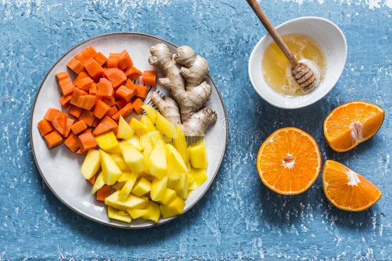 Ingredients for vitamin smoothies - fresh ripe mango, carrot, orange, honey, ginger on a blue background, top view. Detox healthy. Drink stock images