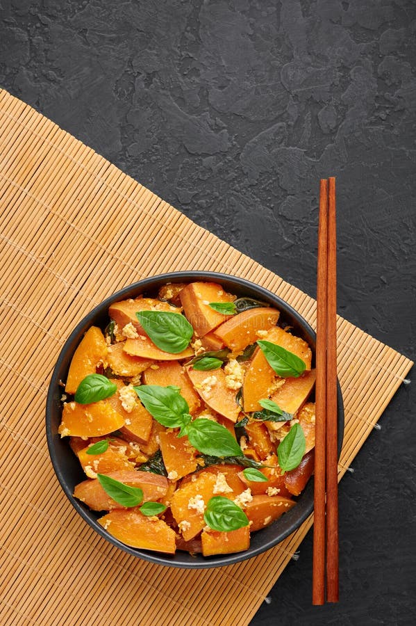 Pad Faktong or Thai Stir-fried Pumpkin in black bowl at dark slate backdrop. Thai Food. Fried squash stock photo
