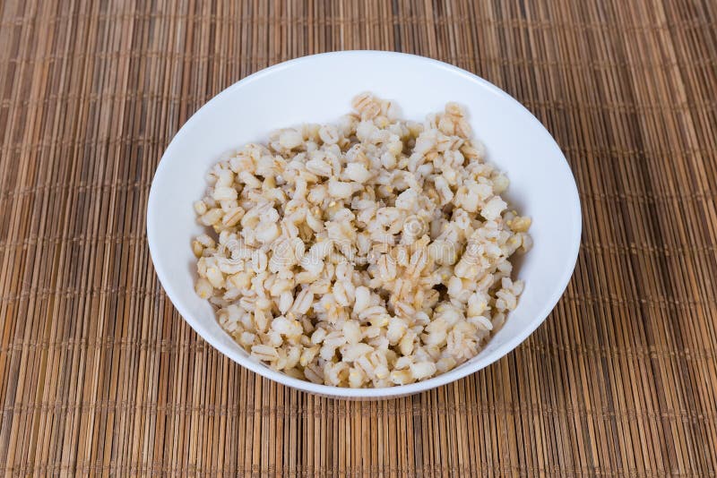 Pearl barley porridge in bowl on bamboo placemat. Pearl barley porridge in the white bowl on the bamboo table mat royalty free stock photos