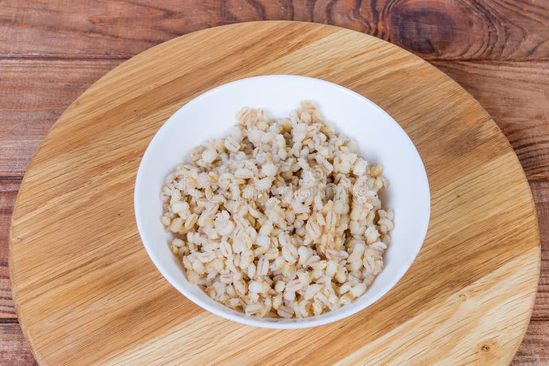 Pearl barley porridge in bowl on wooden surface. Pearl barley porridge in the white bowl on the wooden surface royalty free stock images