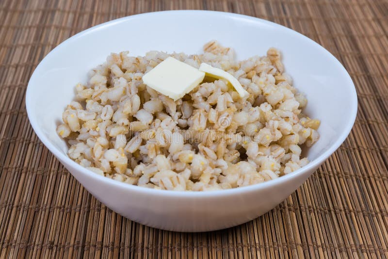 Pearl barley porridge with butter in white bowl close-up. Pearl barley porridge with butter pieces in the white bowl on the bamboo table mat, close-up in royalty free stock images