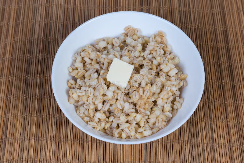 Pearl barley porridge with butter in white bowl. Pearl barley porridge with butter piece in the white bowl on the bamboo table mat stock images