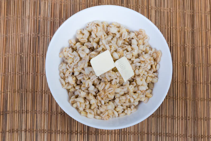Pearl barley porridge with butter in white bowl, top view. Pearl barley porridge with butter pieces in the white bowl on the bamboo table mat, top view stock images