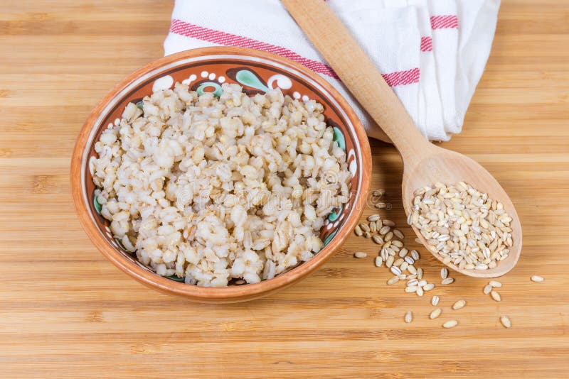 Pearl barley porridge in bowl and uncooked pearl barley groats. Pearl barley porridge in the clay glazed bowl and uncooked pearl barley groats in the wooden royalty free stock photography
