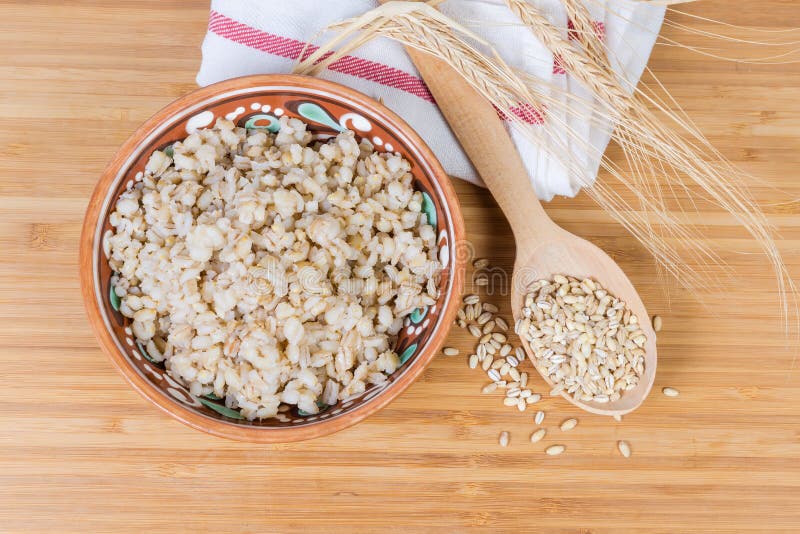 Pearl barley porridge, uncooked groats and barley ears, top view. Pearl barley porridge in the clay glazed bowl, uncooked groats in the wooden spoon and barley stock photo