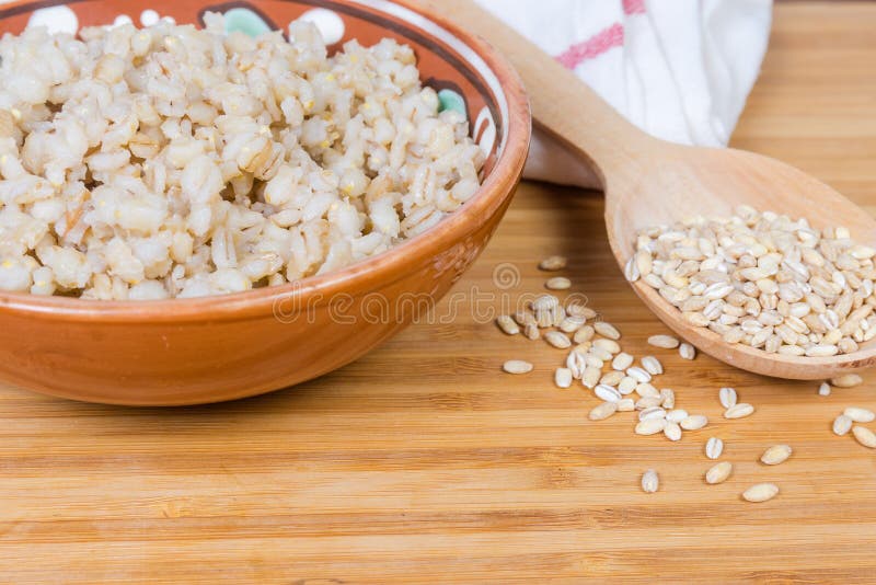 Pearl barley porridge and uncooked pearl barley groats, fragment closeup. Pearl barley porridge in the clay glazed bowl and uncooked pearl barley groats in the stock images