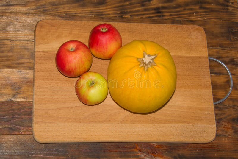 Ripe red apples and pumpkin on a wooden chopping Board with iron handle. Dark rustic background. Autumn composition stock photo