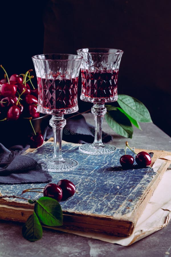 Two glass with a red alcoholic drink, old books and ripe cherry berries on a black background. Still life with red wine, ripe. Cherries and books stock images