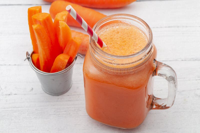 Vitamin and mineral rich liquid nourishment, natural antioxidant and refreshing drink concept with glass of carrot juice and raw. Carrots isolated on white wood royalty free stock photography