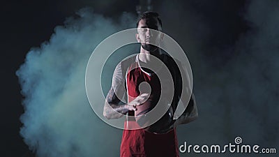 Portrait bearded young brutal confident basketball player stand with a ball in the clouds of smoke on black background. stock footage