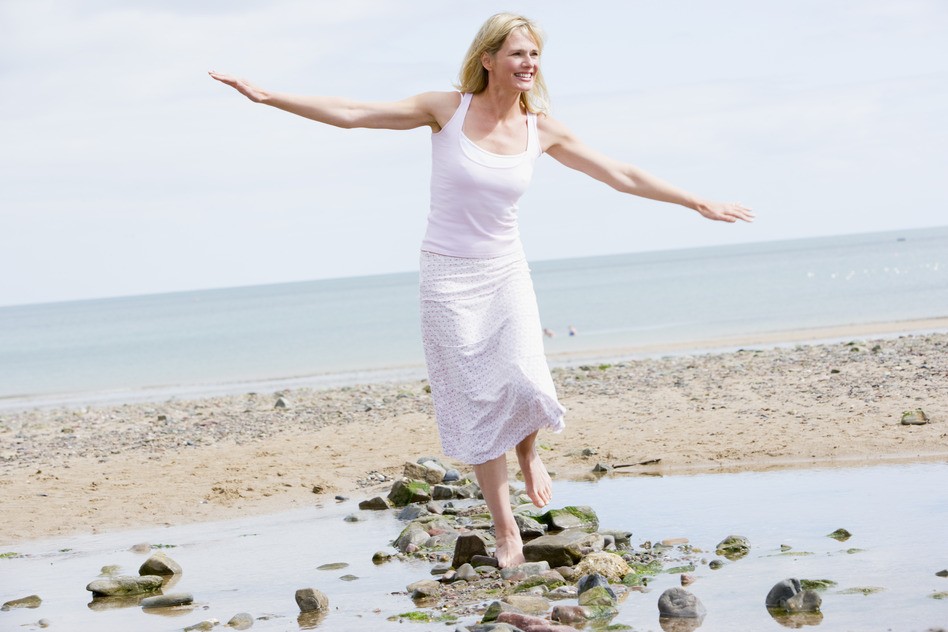 happy woman walking along beach balancing on rocks