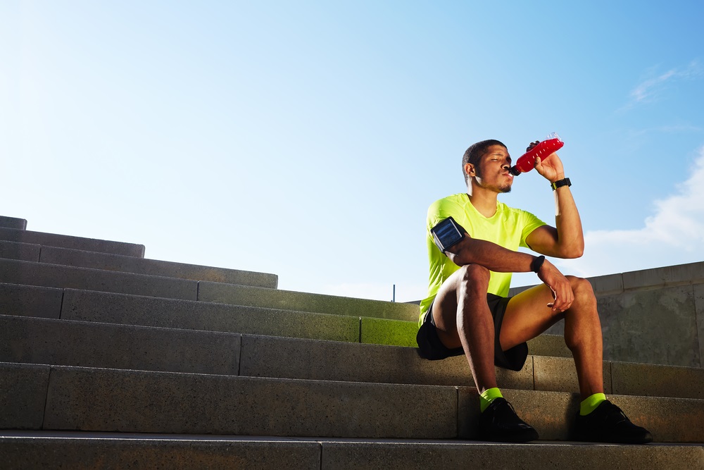 Man in exercise gear sitting on steps drinking a sports drink